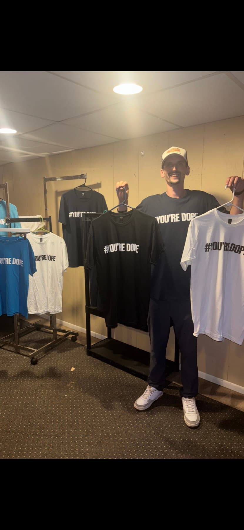 White, black, and blue YOU’RE DOPE shirts on a rack