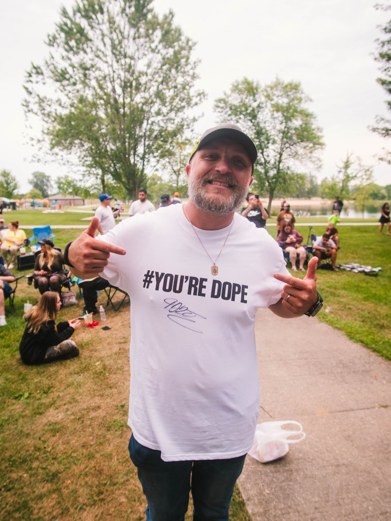 A man outdoors pointing at the #YOU’RE DOPE print on his shirt